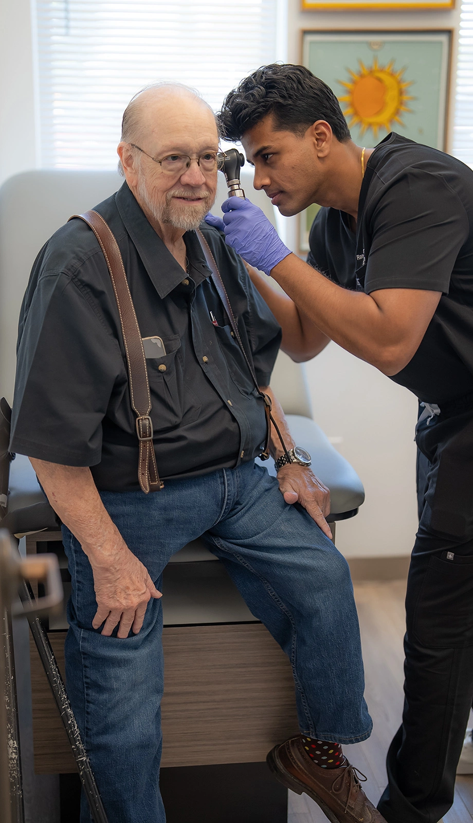 Dr. Rangish Yuvaraj examining an older man's ear with an otoscope during an office visit