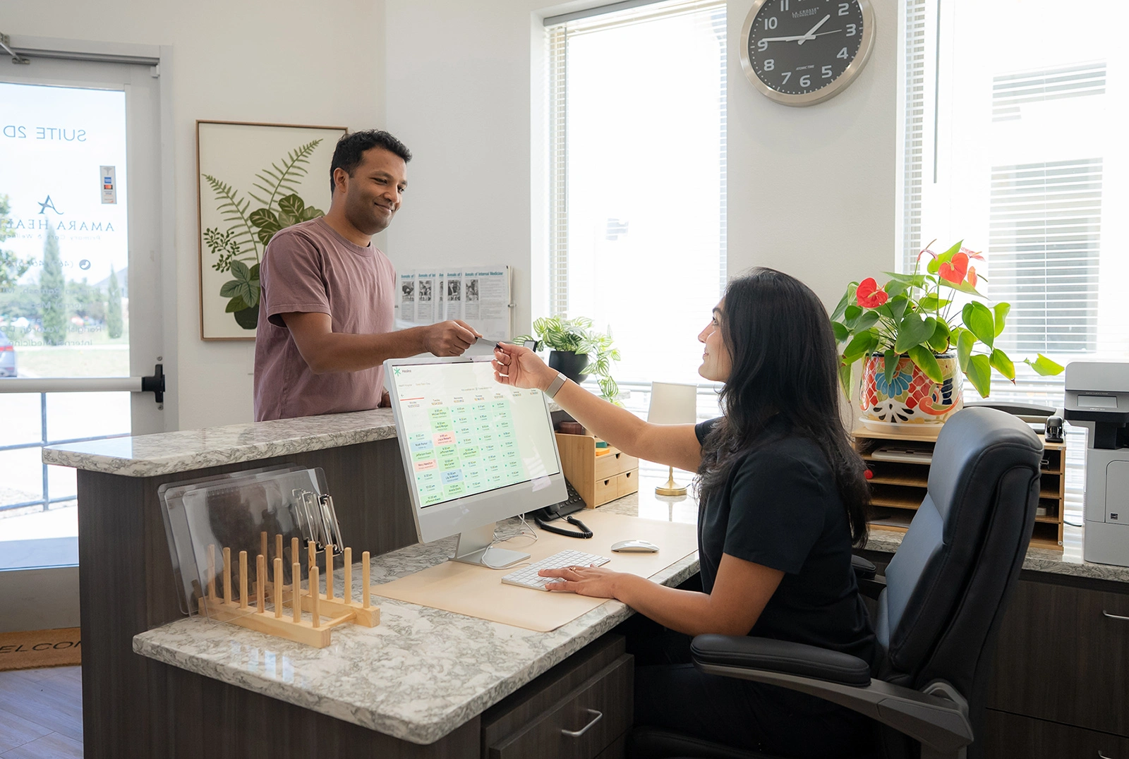 A man at the front desk handing a card to a member of the Amara Health team.