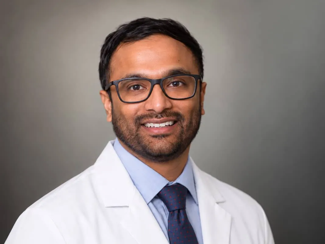Dr. Koushik Kasanagottu in a white coat over scrubs, photographed in a hospital corridor.
